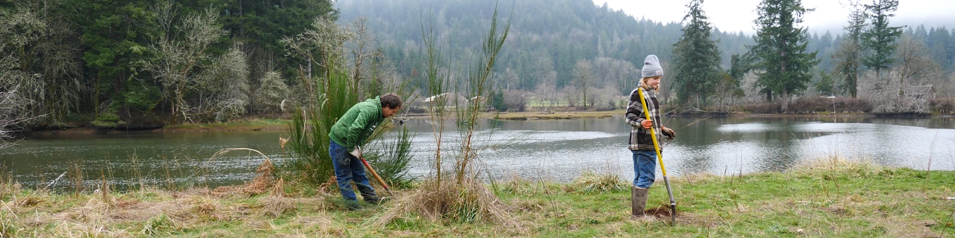 Two people planting along a body of water.